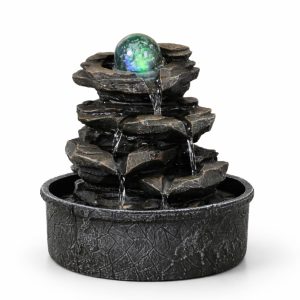 Fontaine d'interieur cascade en pierre sombre avec boule de verre lumineuse verte et bleue en haut